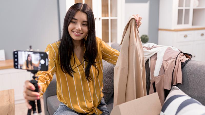 female vlogger at home with smartphone unboxing clothes
